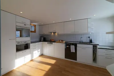 a white kitchen with white cabinets and a wooden floor at Undereggli in Nesslau