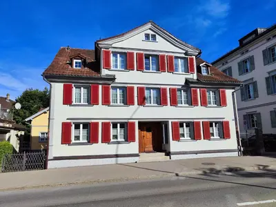 a large white building with red shutters on a street at Dein Zuhause in Herisau in Herisau