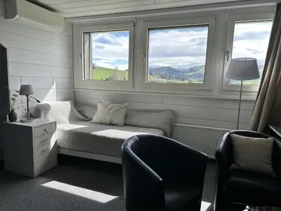 a room with a bed and a chair and two windows at Hotel Säntis Teufen in Teufen