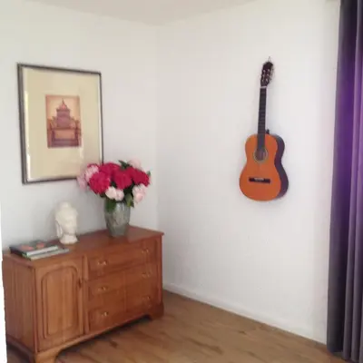a guitar hanging on a wall next to a dresser with flowers at Konstanz nähe, ruhiges 4-Zim-Wohnung bis 8 Personen in Kreuzlingen