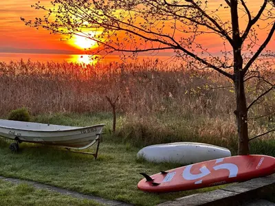 a boat and a canoe on the grass with the sunset at Haus am Seeufer mit Veranda in natürlicher Umgebung in Güttingen