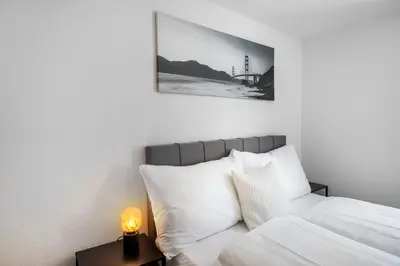 a bed with white sheets and a picture on the wall at book2stay modernes Apartment OLMA-Areal in St. Gallen