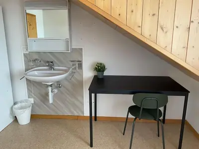 a bathroom with a sink and a table with a chair at 25 - Gästehaus Erika - Hundwil - Appenzellerland in Hundwil
