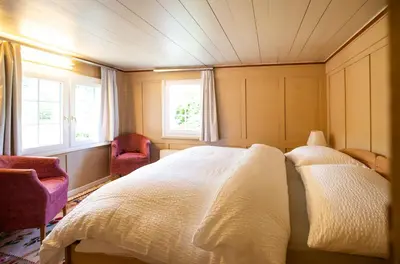 a bedroom with a bed with two chairs and two windows at Wohnhaus Münzmühle in Appenzell in Appenzell