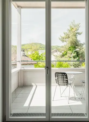 a sliding glass door with a chair on a balcony at Gästehaus Meiersegg - HotelFlawil in Flawil