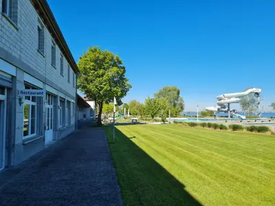a grass field next to a building with a tree at Herberge Seeperle Bistro Rorschach in Rorschach