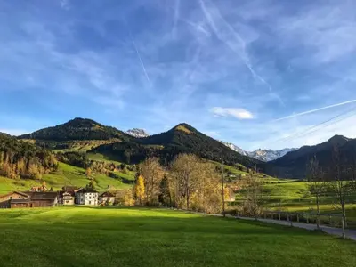 a green field with a house and mountains in the background at Apartment im Dorf Urnäsch by Interhome in Urnäsch