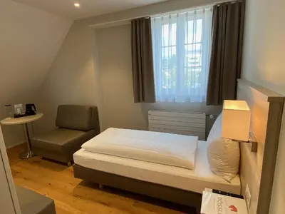 a small bedroom with a bed and a chair at Hotel Garni Rössli in St. Gallen