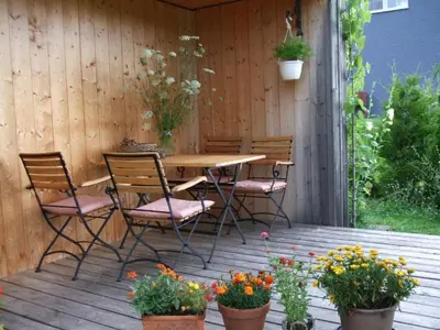 a wooden deck with a table and chairs and flowers at Apartment Ballmoos Ferienwohnung by Interhome in Gais