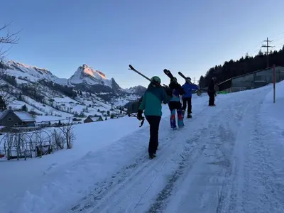 a group of people walking down a snow covered road with skis at Apartment Terrasse & Pistenähe by Interhome in Alt Sankt Johann