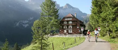 two people riding bikes down a path in front of a house at Berggasthaus Voralp in Grabs