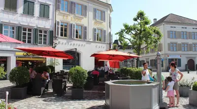 a group of people standing in a courtyard with umbrellas at Hotel Le Lion - Self Check-in in Bischofszell