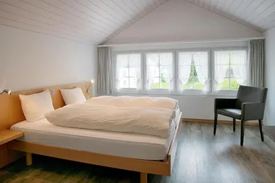 a bedroom with a bed and a chair and windows at Loosmühle in Weissbad