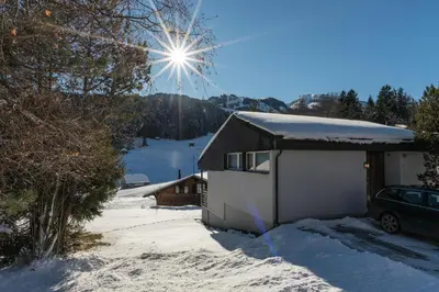 a snow covered house with the sun shining behind it at Chalet Pfiff in Wildhaus