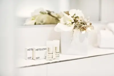 a shelf with moisturizers and flowers in a bathroom at Hotel Schäfli in Uzwil