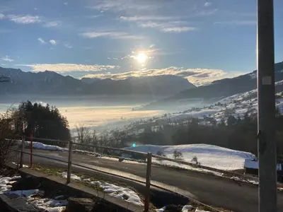 a view of a snow covered valley with the sun at Ferienwohnung Haus am Bach in Toggenburg in Wildhaus