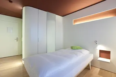 a bed in a room with a white wall at Hotel Dom, zentral - herzlich - sozial engagiert in St. Gallen