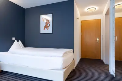 a bedroom with a large white bed with a blue wall at Self Check-In Hotel David 22 in St. Gallen