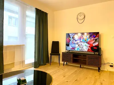 a living room with a television and a clock on the wall at City Center Premium Apartment - Buchs SG in Buchs