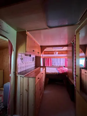 a kitchen with wooden cabinets and a bed in the background at Camping Schönengrund in Schönengrund