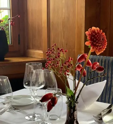 a table with wine glasses and a vase with flowers at Hotel Restaurant Schlössli Sax in Sax