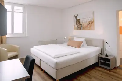 a white bedroom with a bed and a chair at Hotel & Restaurant Nollen in Hosenruck